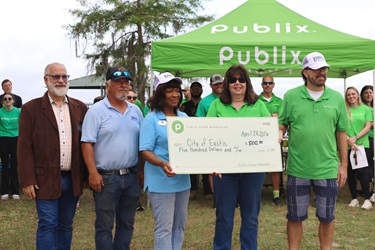 (Left to right) Interim City Manager Rick Gierok, City of Eustis Horticulturist Tim Howard and Eustis Mayor Emily Lee accepting a check from Publix representatives.  