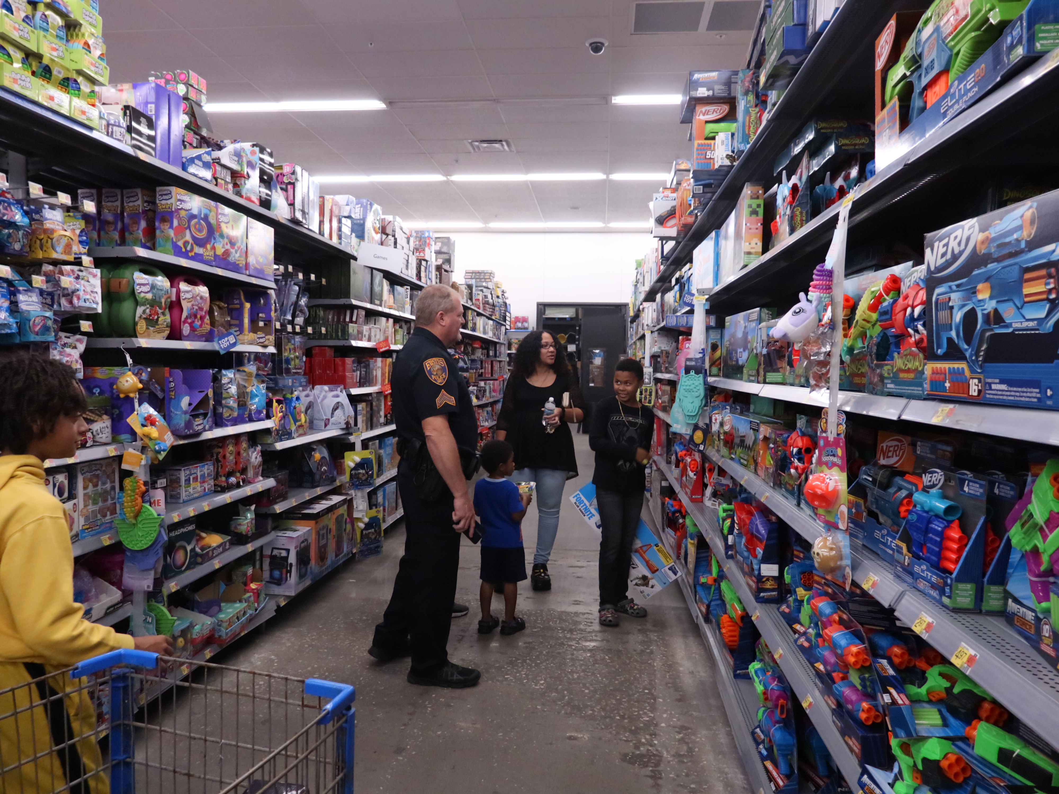 Three children, a women and a police officer are looking through a toy aisle in Walmart.