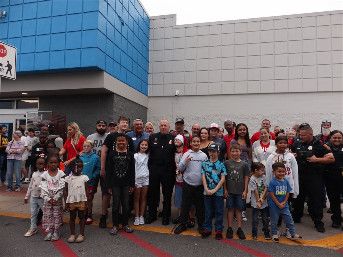 A group of children standing with police officers and the city mayor. They are all standing in front of a Walmart storefront. 